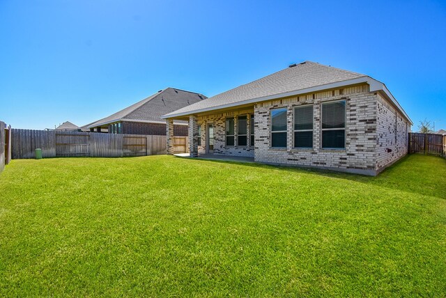 back of house with brick siding, a fenced backyard, a yard, and roof with shingles