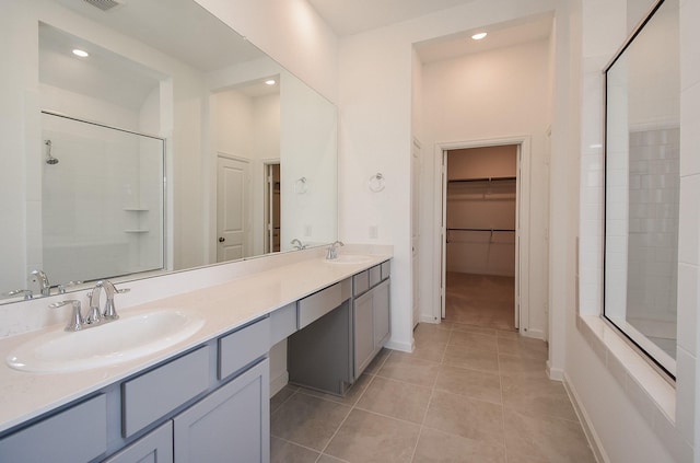 bathroom with a tile shower, tile patterned flooring, double vanity, and a sink