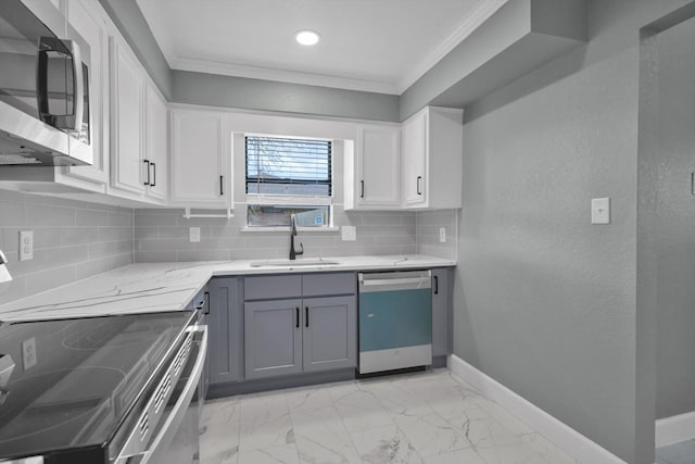 kitchen featuring crown molding, gray cabinets, appliances with stainless steel finishes, a sink, and baseboards