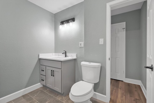 half bathroom with marble finish floor, vanity, toilet, and baseboards