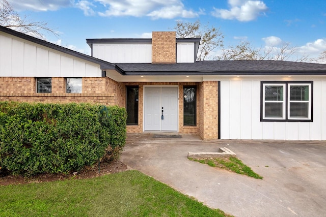 doorway to property with roof with shingles and brick siding