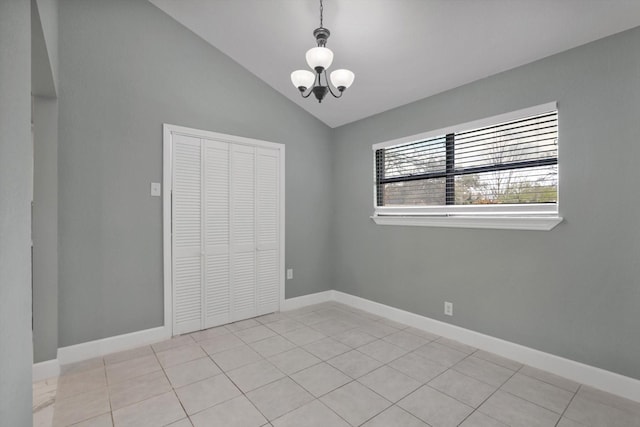 unfurnished bedroom featuring a notable chandelier, light tile patterned floors, a closet, vaulted ceiling, and baseboards