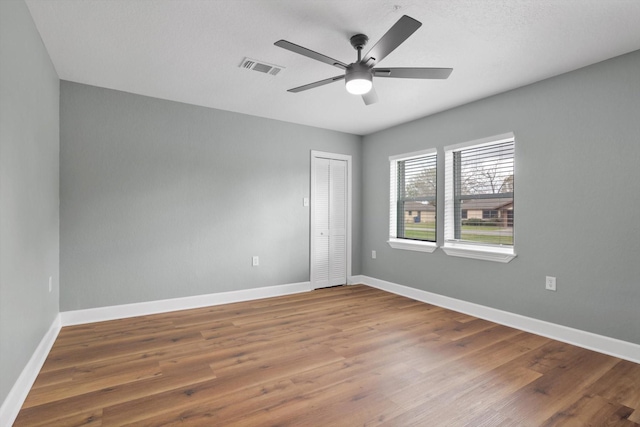 spare room with wood finished floors, visible vents, and baseboards