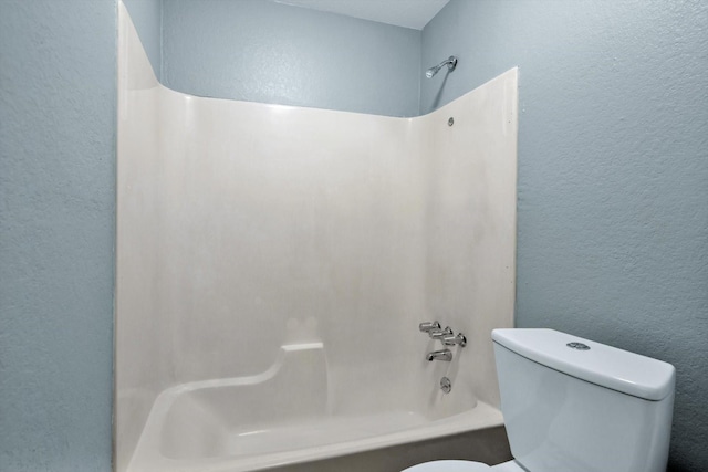 bathroom with a textured wall, shower / washtub combination, and toilet