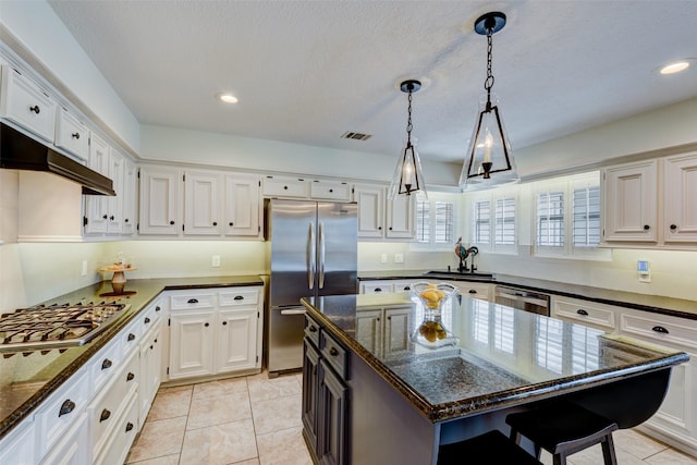 kitchen with stainless steel appliances, white cabinets, a sink, dark stone counters, and under cabinet range hood