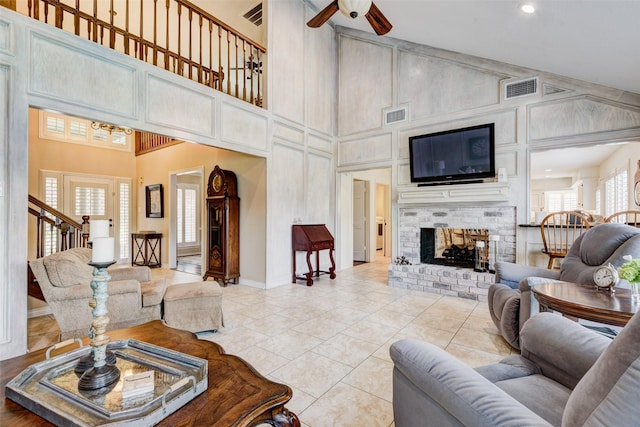 living room with visible vents, a ceiling fan, a fireplace, high vaulted ceiling, and light tile patterned flooring