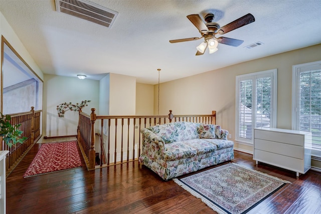 living area featuring a textured ceiling, ceiling fan, wood-type flooring, and visible vents