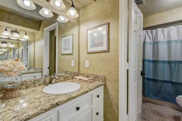 full bath featuring visible vents, a textured wall, vanity, and toilet