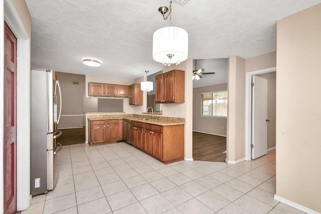 kitchen with light tile patterned floors, stainless steel appliances, brown cabinetry, and a sink