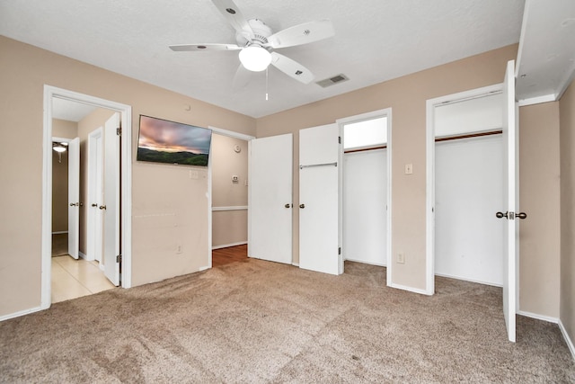 unfurnished bedroom with visible vents, ensuite bathroom, a textured ceiling, carpet flooring, and two closets