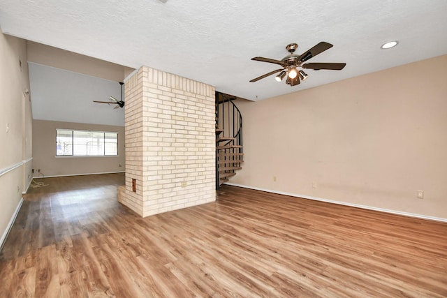 unfurnished living room featuring stairway, a ceiling fan, a textured ceiling, wood finished floors, and baseboards