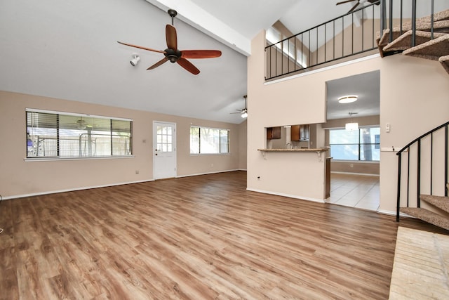 unfurnished living room featuring stairway, wood finished floors, a ceiling fan, and a healthy amount of sunlight