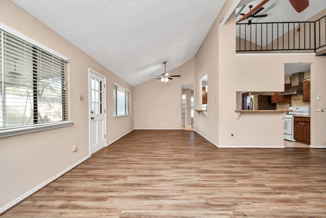 unfurnished living room with a ceiling fan, light wood-style floors, a textured ceiling, high vaulted ceiling, and baseboards