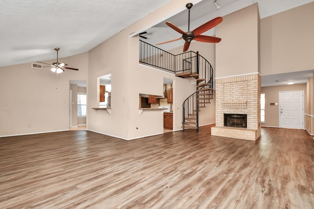 unfurnished living room featuring ceiling fan, a fireplace, wood finished floors, visible vents, and vaulted ceiling