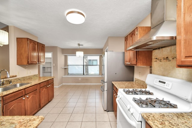 kitchen featuring brown cabinets, light tile patterned floors, a sink, wall chimney range hood, and white gas range oven