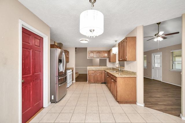 kitchen featuring brown cabinets, a sink, stainless steel refrigerator with ice dispenser, and gas range gas stove