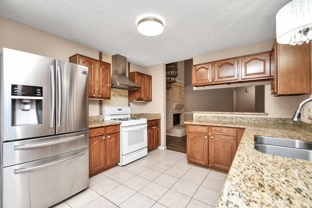 kitchen with light tile patterned floors, a sink, wall chimney exhaust hood, gas range gas stove, and stainless steel fridge