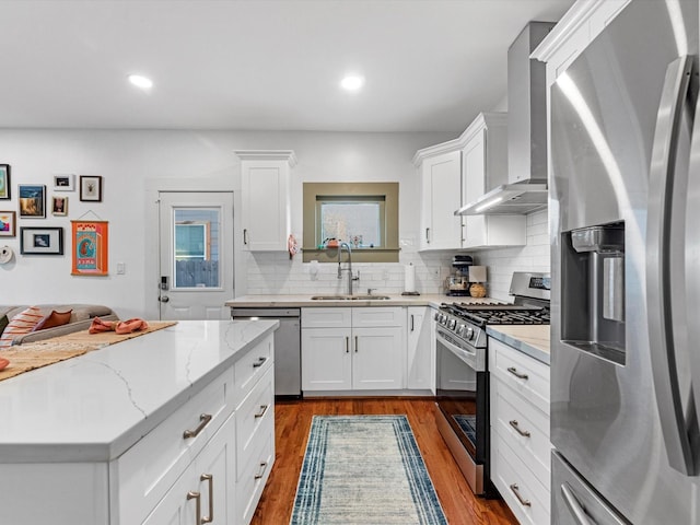 kitchen with stainless steel appliances, decorative backsplash, dark wood-type flooring, a sink, and wall chimney range hood