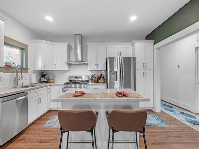 kitchen with a kitchen breakfast bar, stainless steel appliances, wall chimney range hood, white cabinetry, and a sink