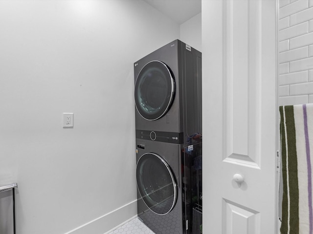 laundry area with tile patterned flooring, stacked washer and clothes dryer, baseboards, and laundry area