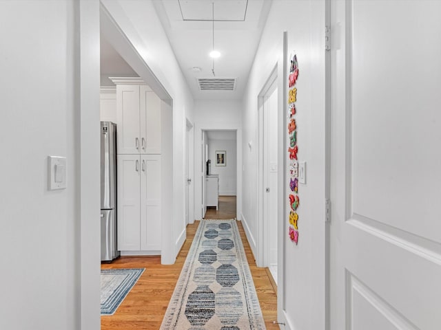 corridor with light wood-type flooring, attic access, visible vents, and baseboards