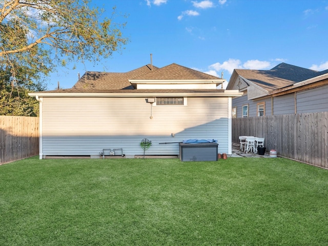 rear view of house featuring a fenced backyard, a shingled roof, and a yard