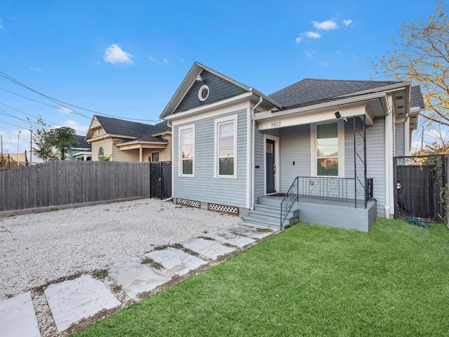 view of front of property with a front yard, covered porch, roof with shingles, and fence