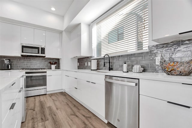 kitchen with stainless steel appliances, a sink, white cabinets, light wood finished floors, and modern cabinets