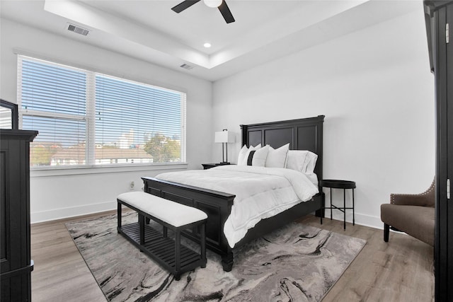 bedroom featuring a tray ceiling, wood finished floors, visible vents, and baseboards