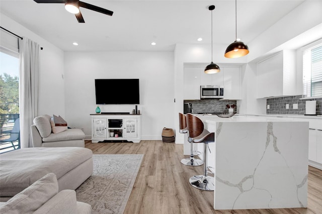 living area with recessed lighting, ceiling fan, light wood-style flooring, and baseboards