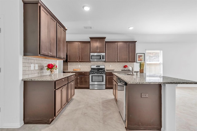 kitchen with appliances with stainless steel finishes, backsplash, a sink, and light stone counters