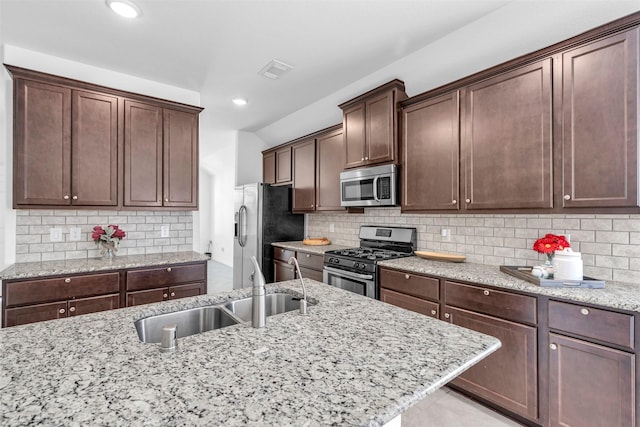 kitchen with tasteful backsplash, visible vents, light stone counters, stainless steel appliances, and a sink