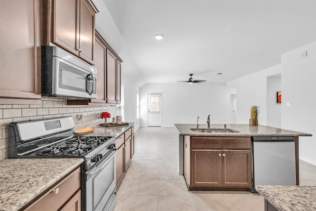 kitchen with a center island with sink, stainless steel appliances, tasteful backsplash, a ceiling fan, and a sink