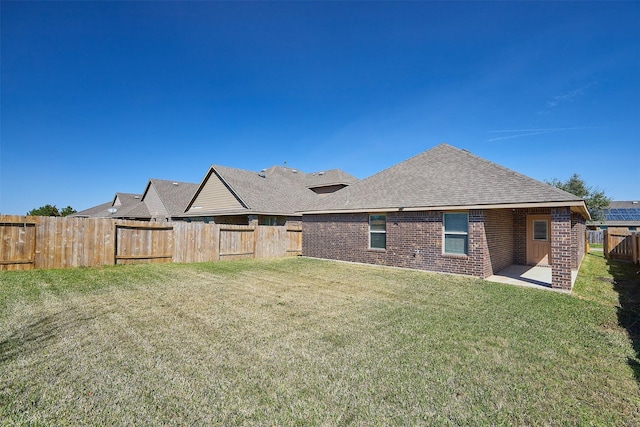 back of house with brick siding, roof with shingles, a lawn, a patio area, and a fenced backyard