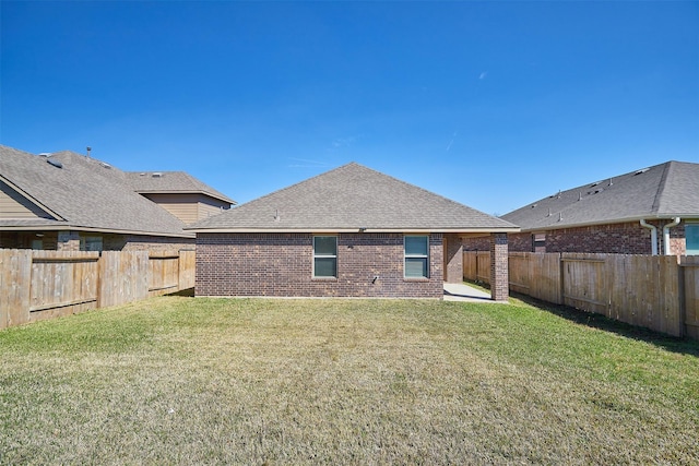 rear view of house with brick siding, a lawn, a shingled roof, and a fenced backyard