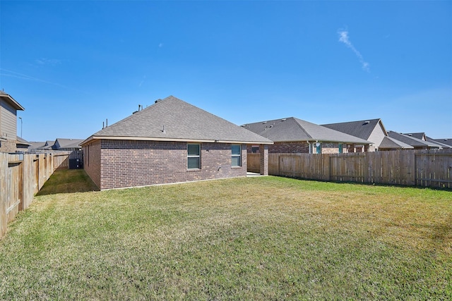 rear view of house with a shingled roof, brick siding, a yard, and a fenced backyard