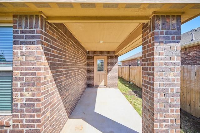 view of exterior entry with fence and brick siding