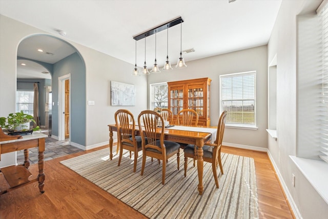 dining space with arched walkways, baseboards, visible vents, and light wood-style floors