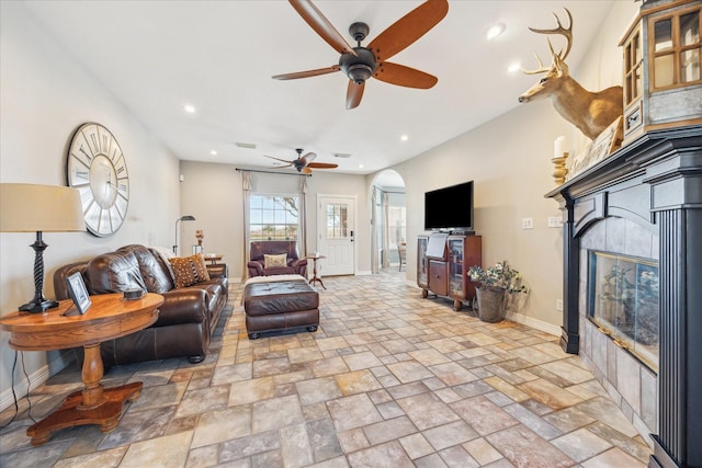 living room with arched walkways, stone finish flooring, baseboards, and recessed lighting