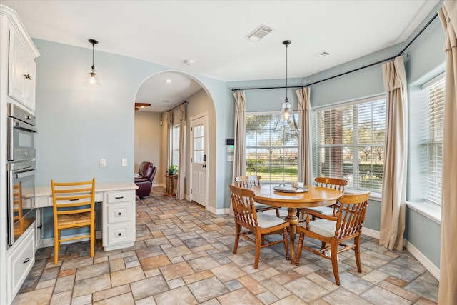 dining space featuring stone finish flooring, visible vents, arched walkways, and baseboards