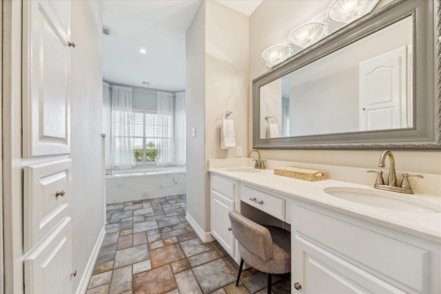 full bath featuring a bathing tub, a sink, stone tile floors, and double vanity