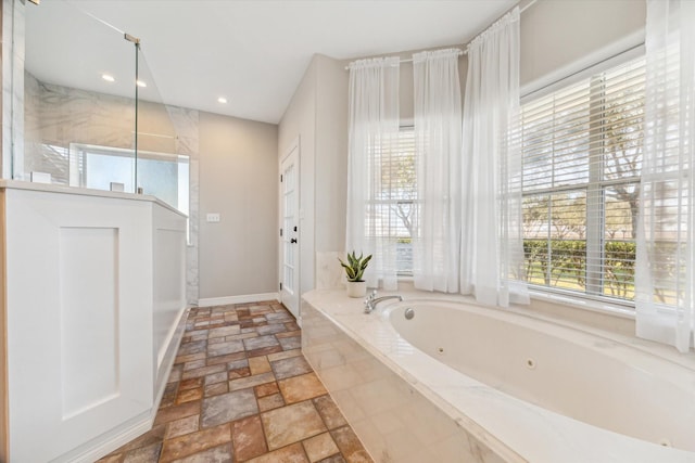 bathroom featuring baseboards, a tub with jets, stone tile flooring, a walk in shower, and recessed lighting