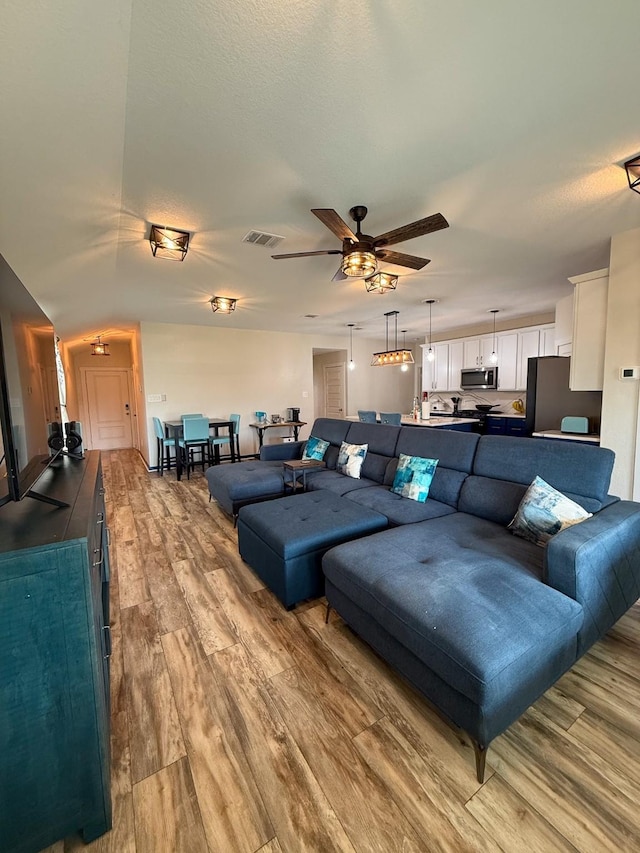 living room featuring ceiling fan, a textured ceiling, wood finished floors, and visible vents