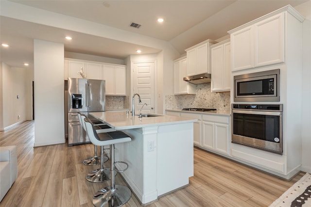 kitchen with visible vents, under cabinet range hood, light wood-style flooring, stainless steel appliances, and a sink