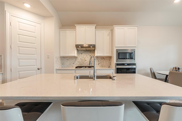 kitchen featuring under cabinet range hood, backsplash, appliances with stainless steel finishes, and a kitchen bar