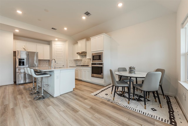 kitchen featuring visible vents, a breakfast bar, white cabinetry, stainless steel appliances, and light wood finished floors