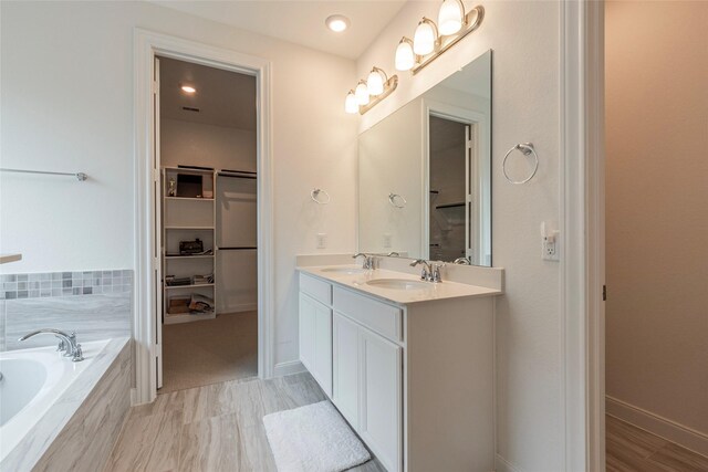 full bath featuring a spacious closet, double vanity, a garden tub, and a sink