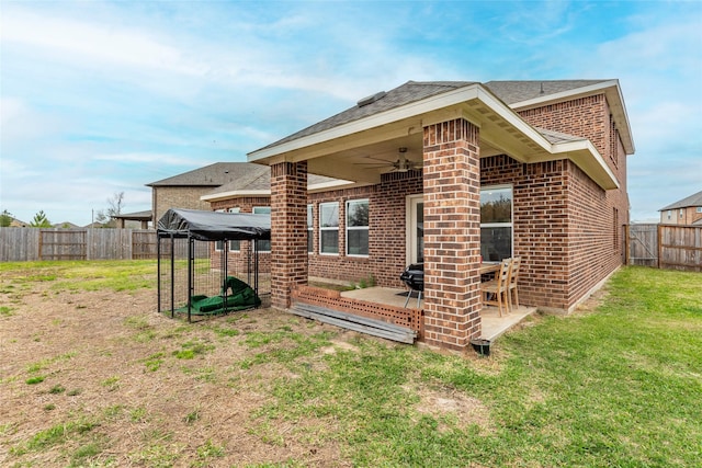 rear view of property featuring brick siding, ceiling fan, a fenced backyard, a yard, and a patio area