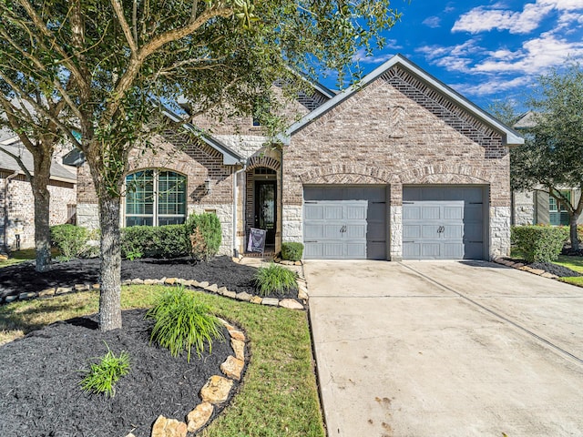 french country style house featuring a garage, concrete driveway, brick siding, and stone siding