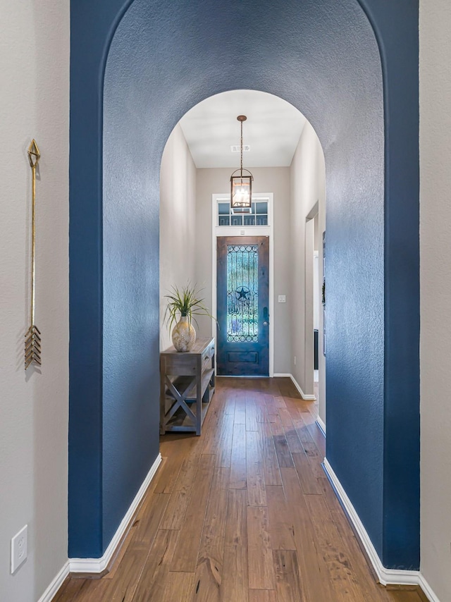 doorway with arched walkways, hardwood / wood-style flooring, and baseboards